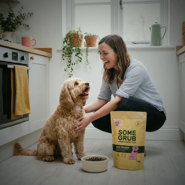 An owner and cockapoo in a kitchen beside a bowl and Some Grub food bag