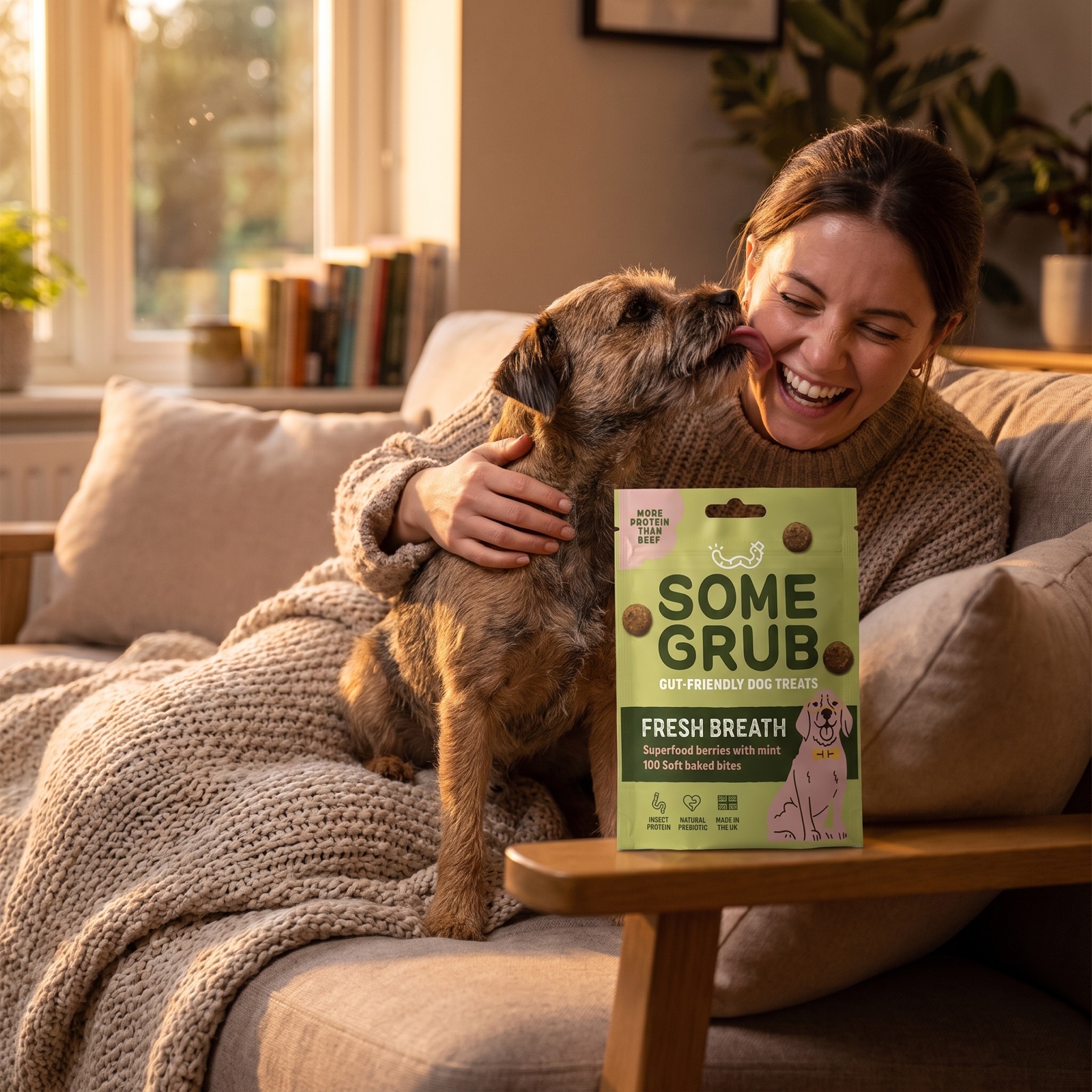 Terrier planting a kiss on its laughing owner's cheek, Fresh Breath pouch on the sofa arm